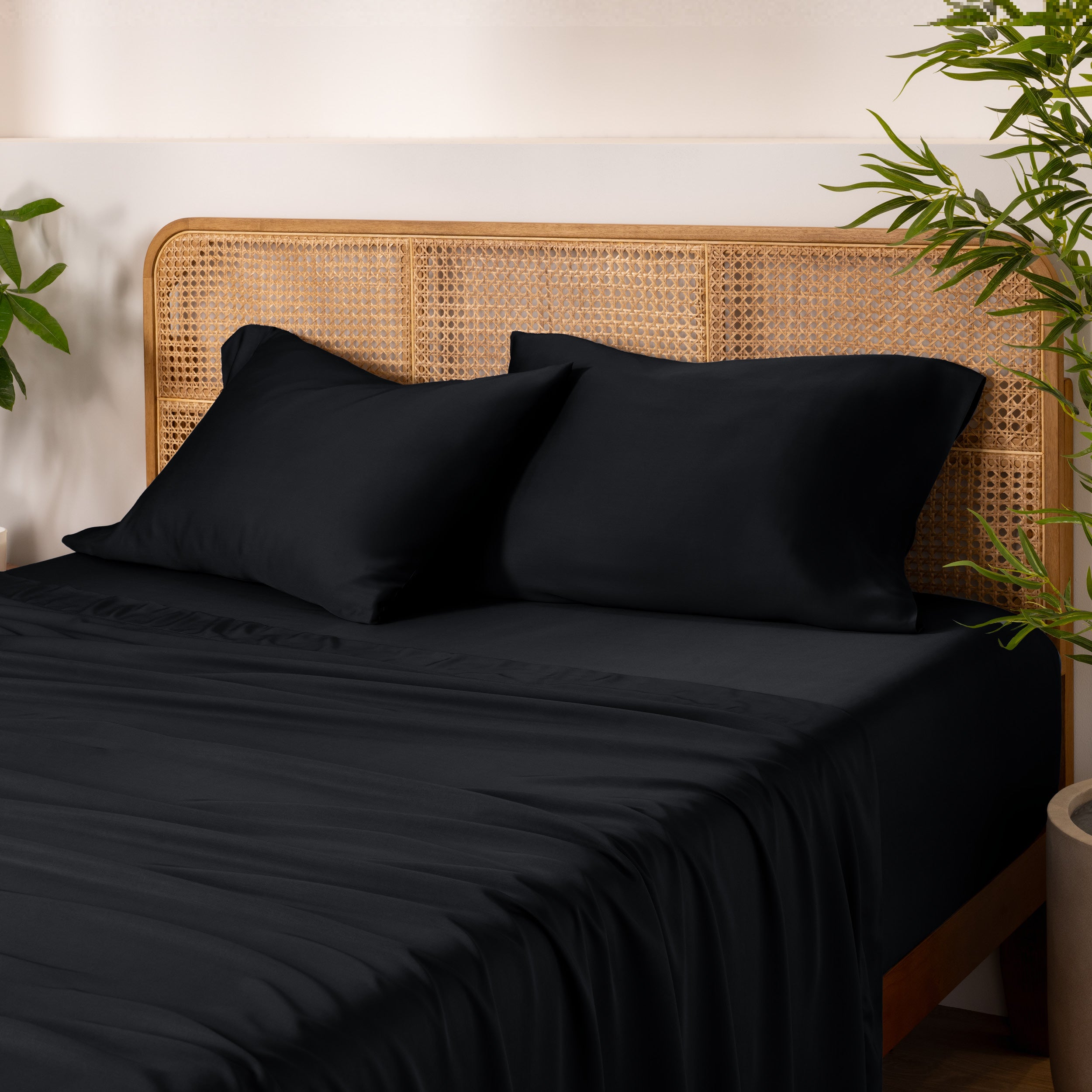 Bamboo bed sheets and pillowcases on a bed with a wicker headboard and plants in the background.