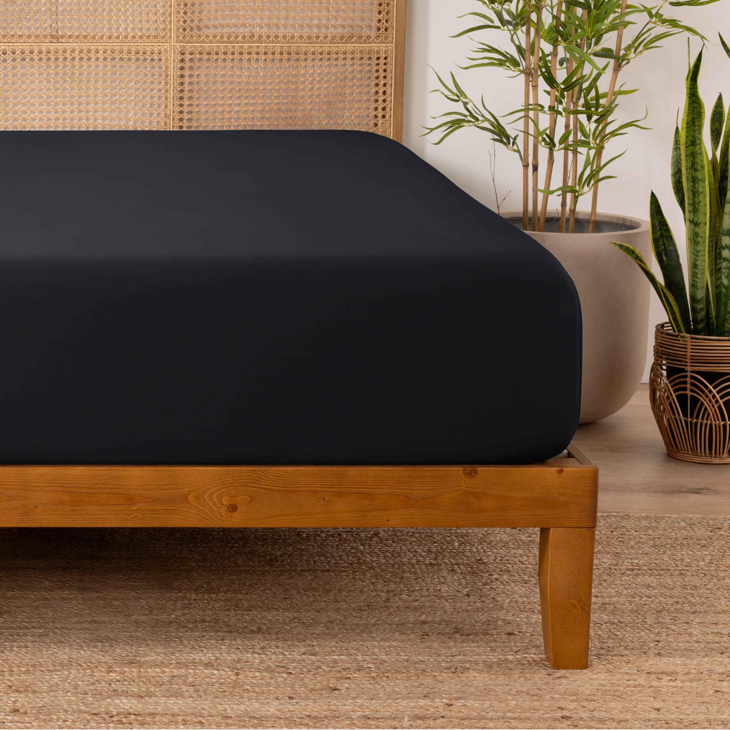 Bamboo fitted sheet on a wooden bed with plants in the background