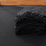 Folded fitted sheet on a bed with a wooden headboard.