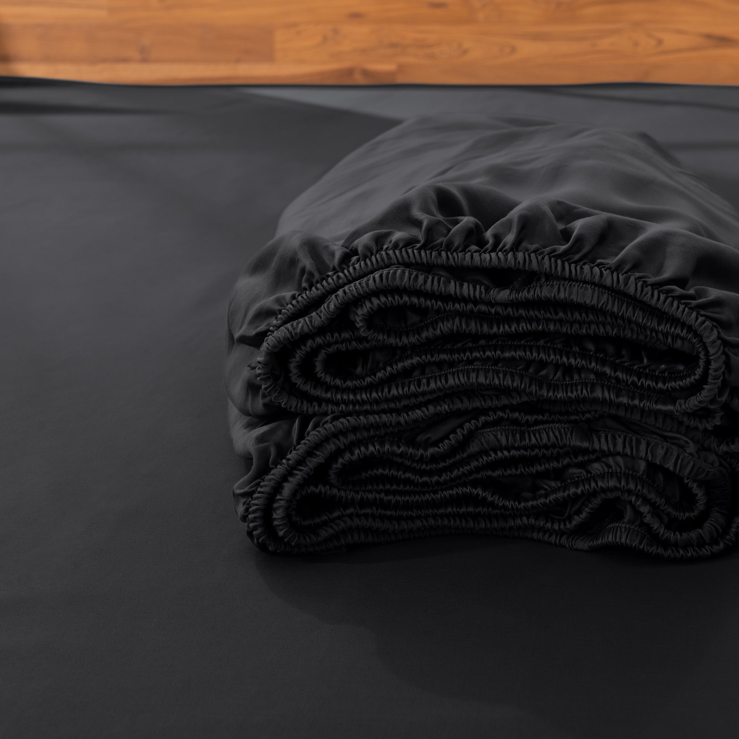 Folded fitted sheet on a bed with a wooden headboard.