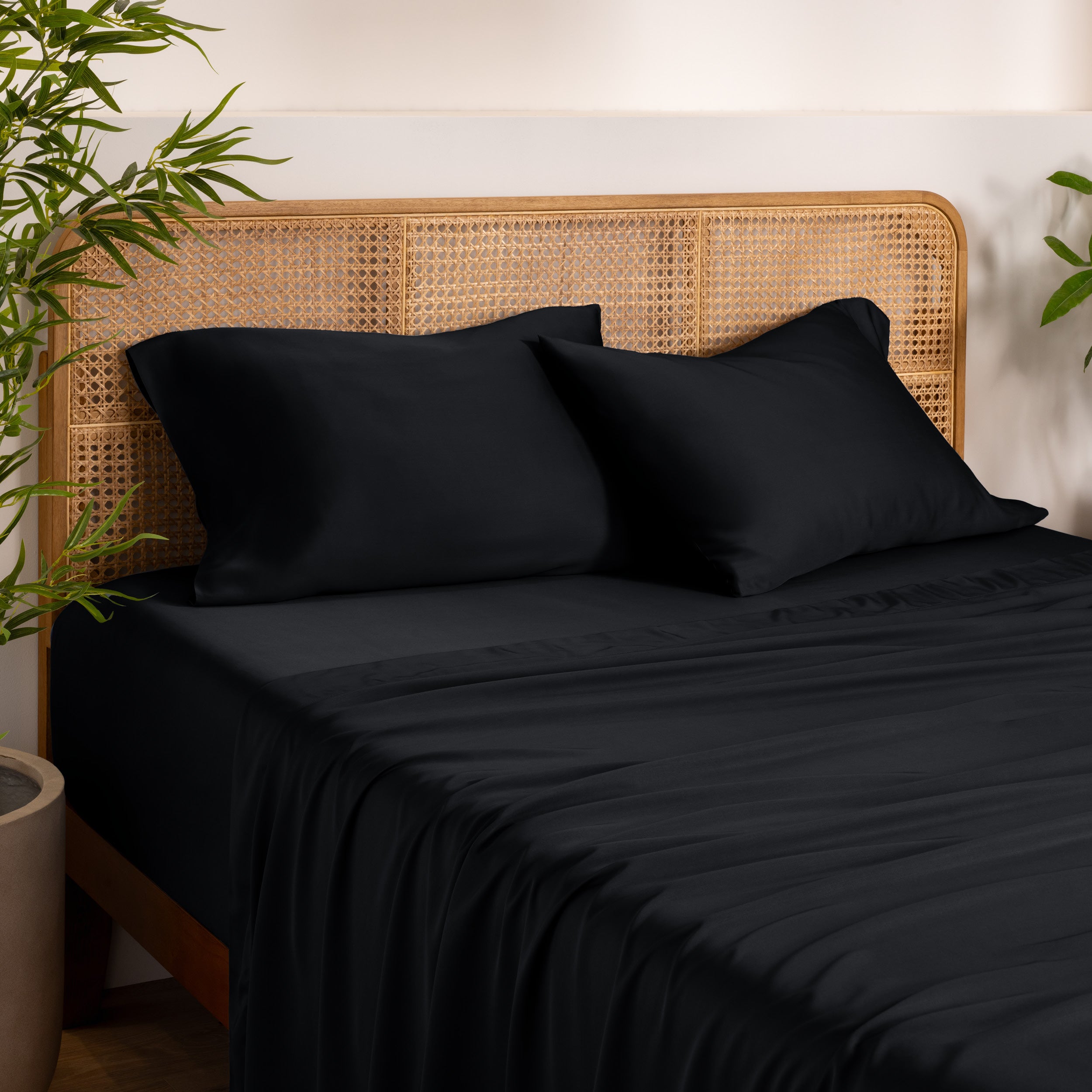 Bamboo bed sheets and pillowcases on a bed with a wicker headboard in a room with plants.