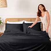 Woman arranging bamboo bedding on a bed with a white wall and plant in the background