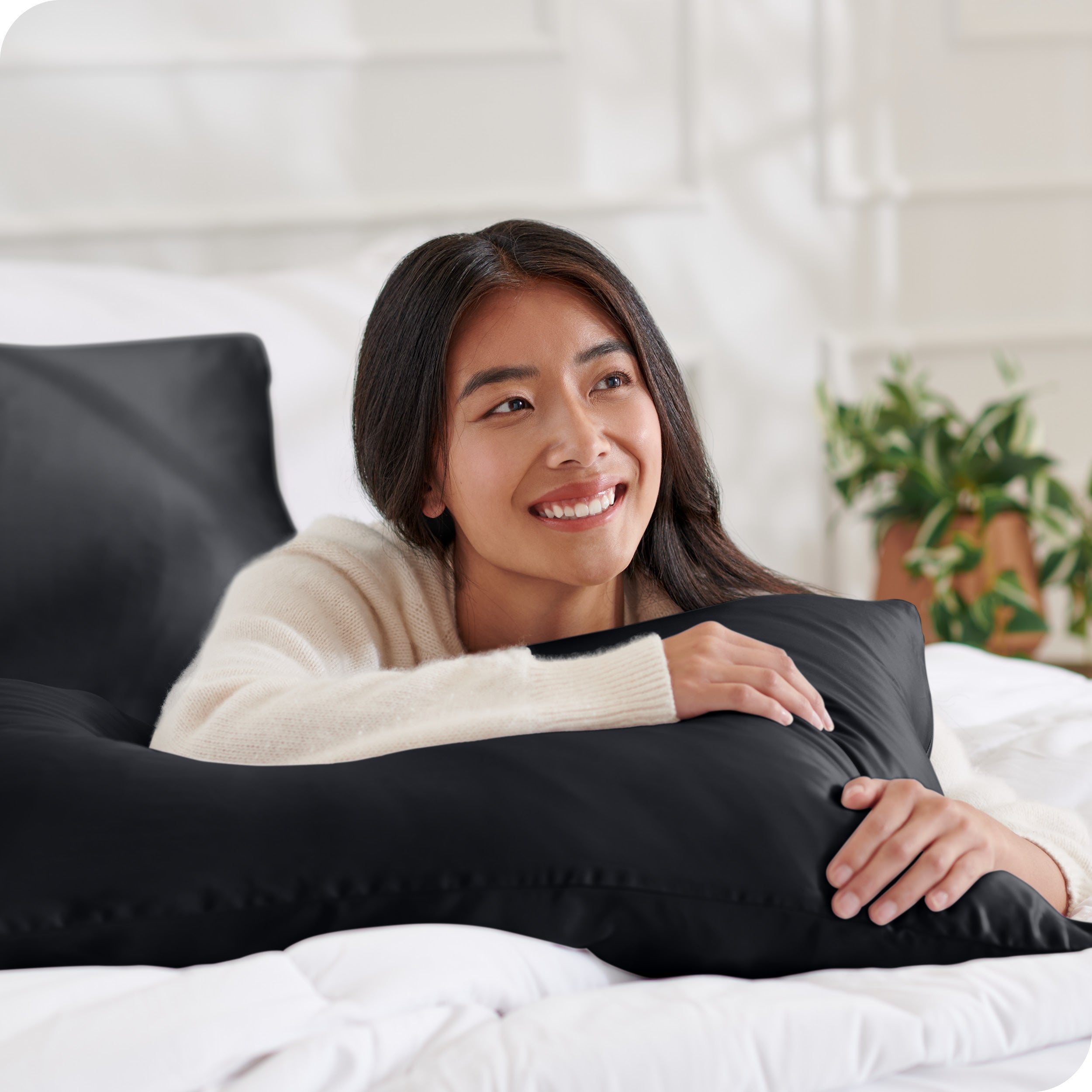 A woman on a bed resting her arm on a silk pillowcase covered pillow