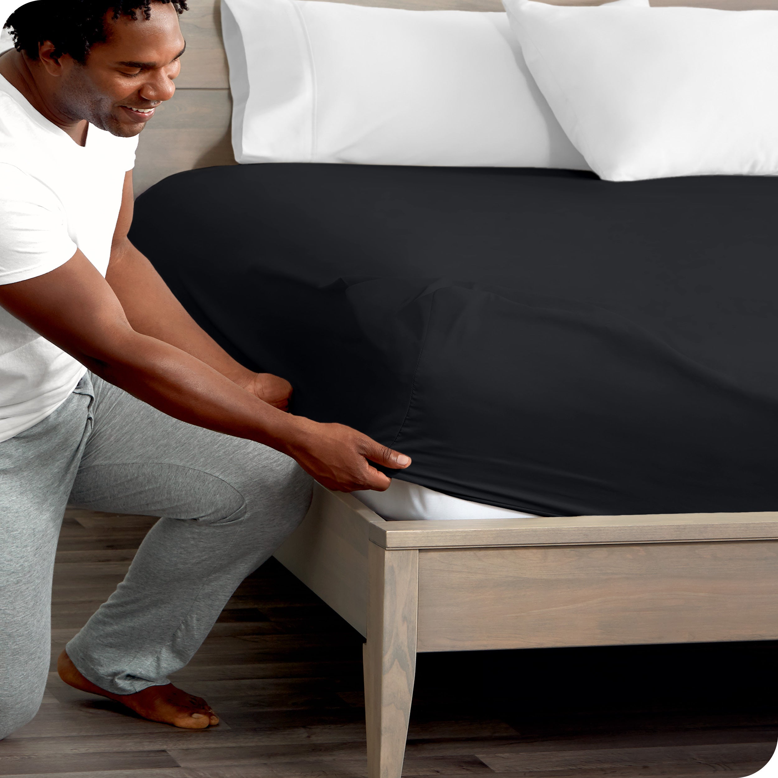 A man kneeling while putting a fitted sheet on a bed