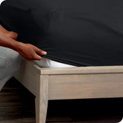 A man is kneeling while putting a fitted sheet on a mattress
