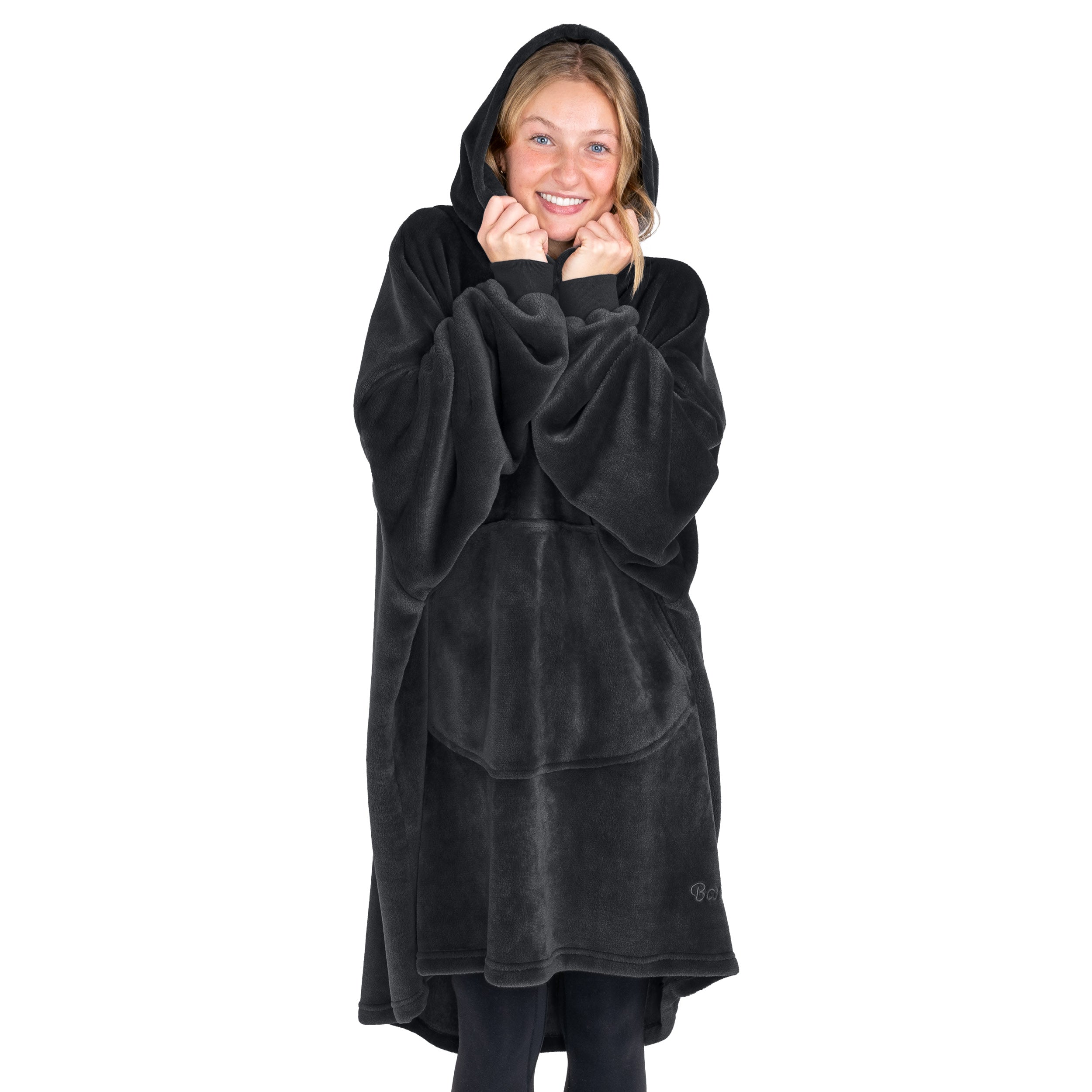 A woman is snuggled up in a hooded microplush wearable blanket