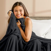 A woman sitting on a bed wrapped in a microplush blanket