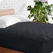 A modern bed with a wooden bed frame with a quilted mattress pad on.
