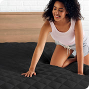A woman is pushed her hand down on a quilted mattress pad on the bed