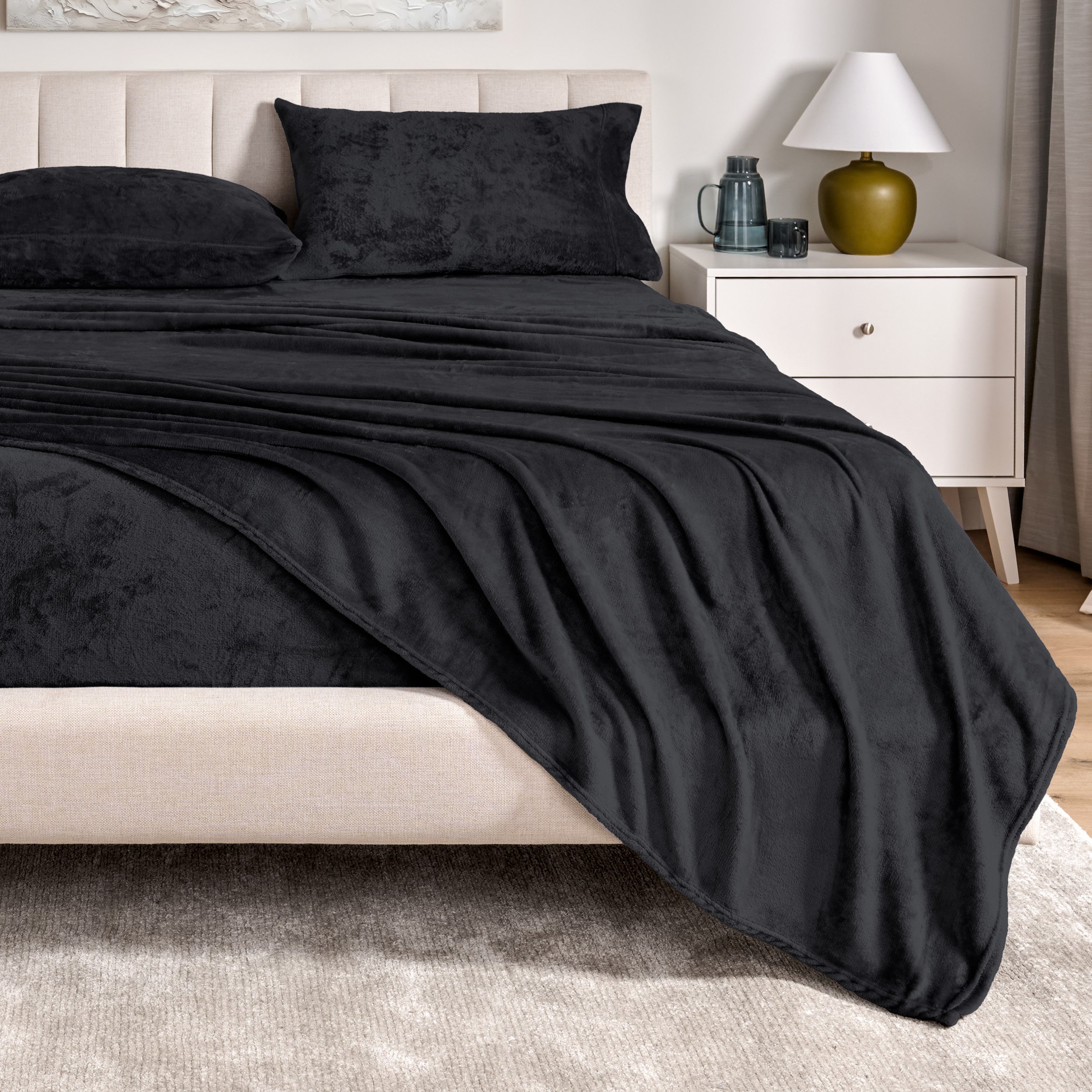 Microplush sheets on a bed in a bedroom setting with a nightstand and lamp.