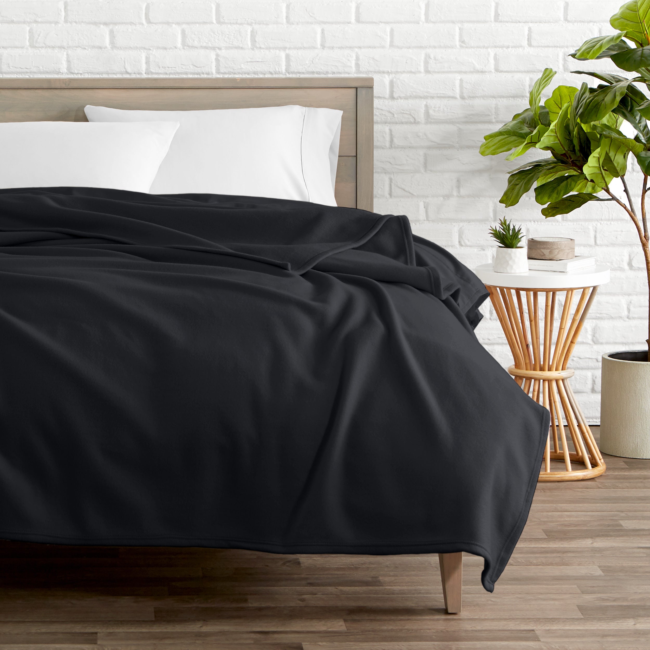 A polar fleece blanket on a bed next to a table and a large plant