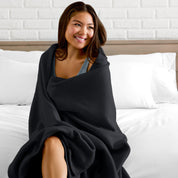 A woman sitting at the end of a bed with a fleece blanket wrapped around her shoulders
