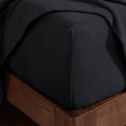 Corner of the bed with a fitted sheet on the mattress and a flat sheet draped over the side and end