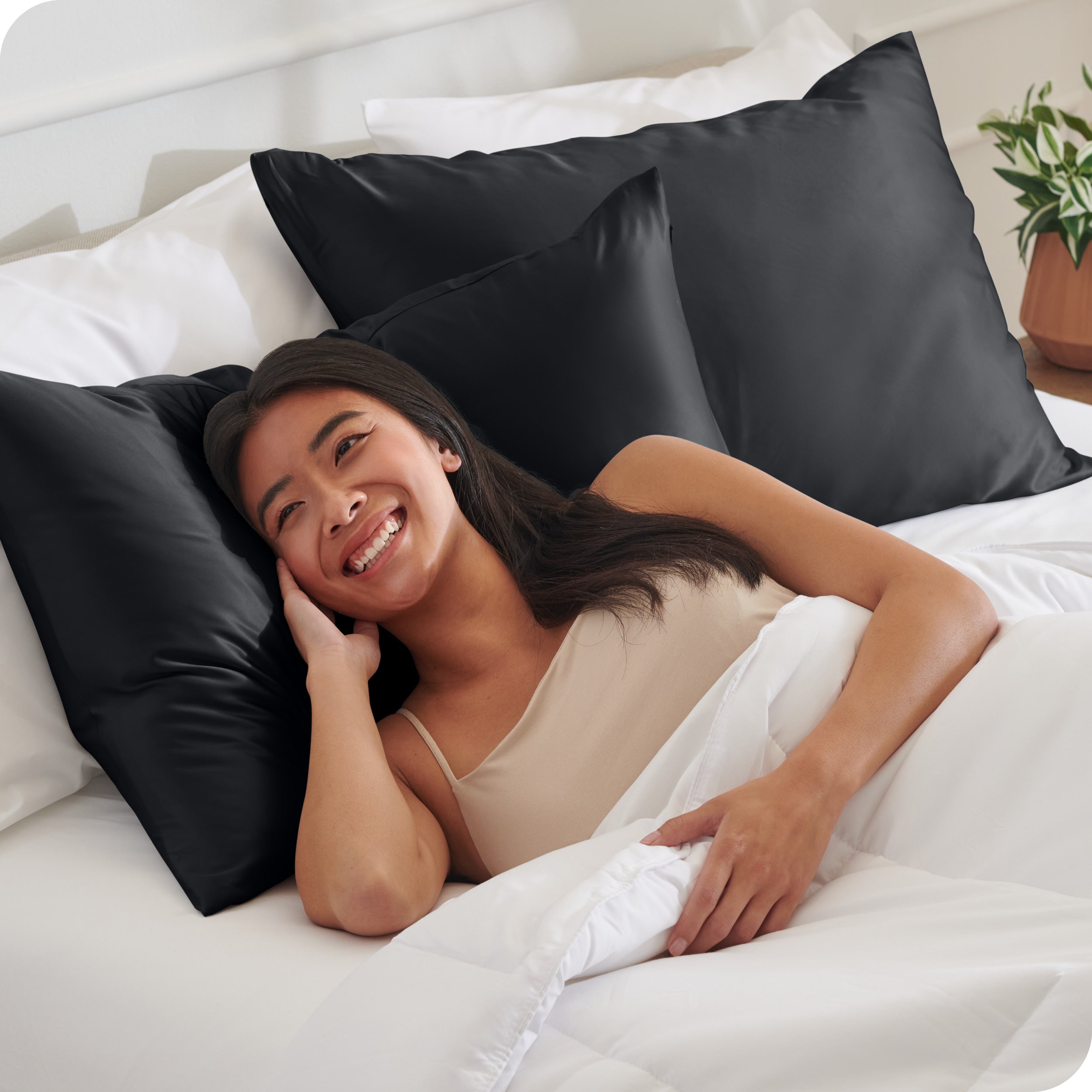 A woman in bed with her head resting on a silk pillowcase covered pillow