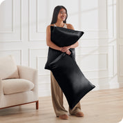 A woman standing while holding 2 pillows with silk pillowcases