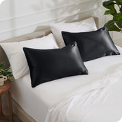 2 satin pillowcases on pillows leaning against other pillows on a bed