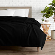 A polar fleece blanket on a bed next to a table and a large plant