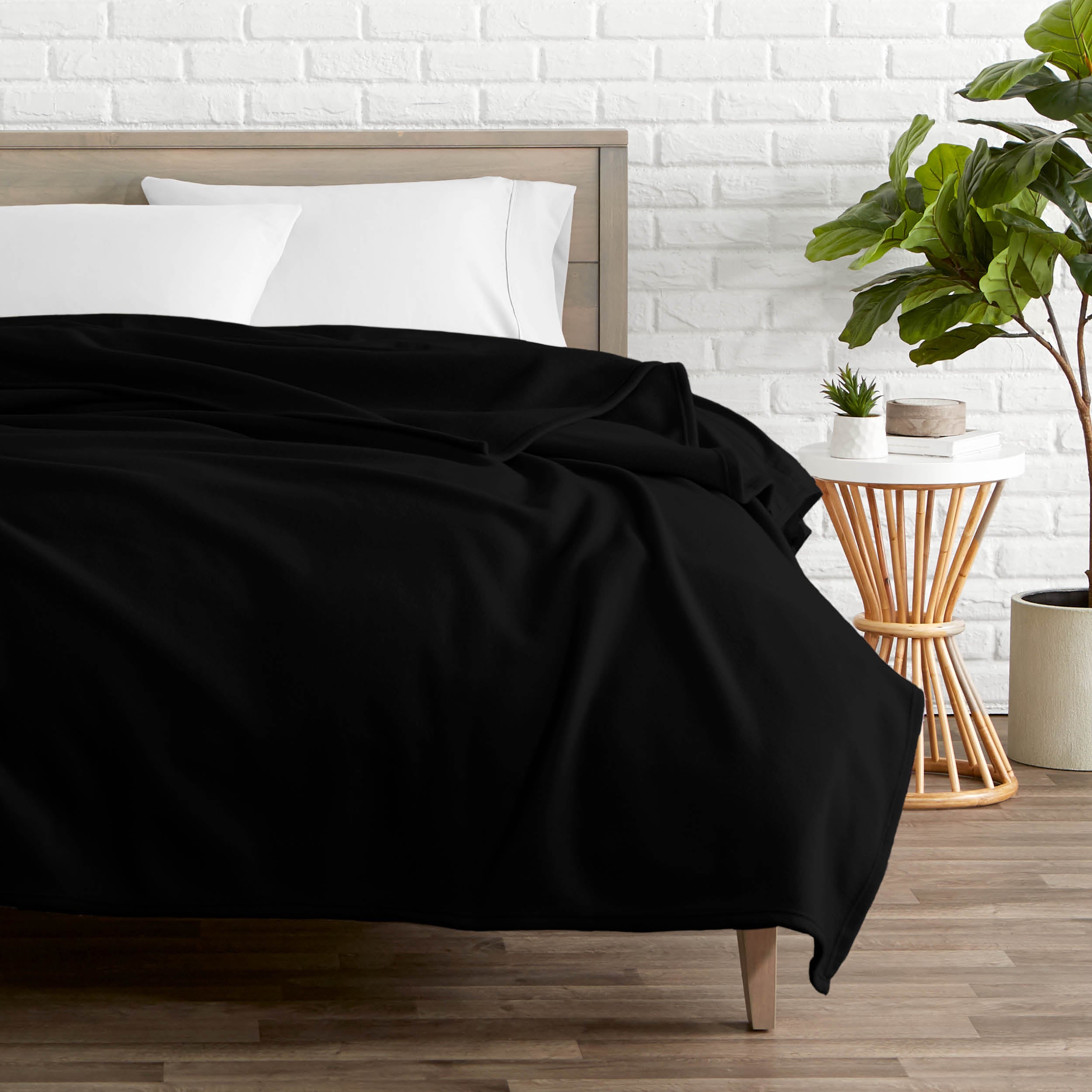A polar fleece blanket on a bed next to a table and a large plant