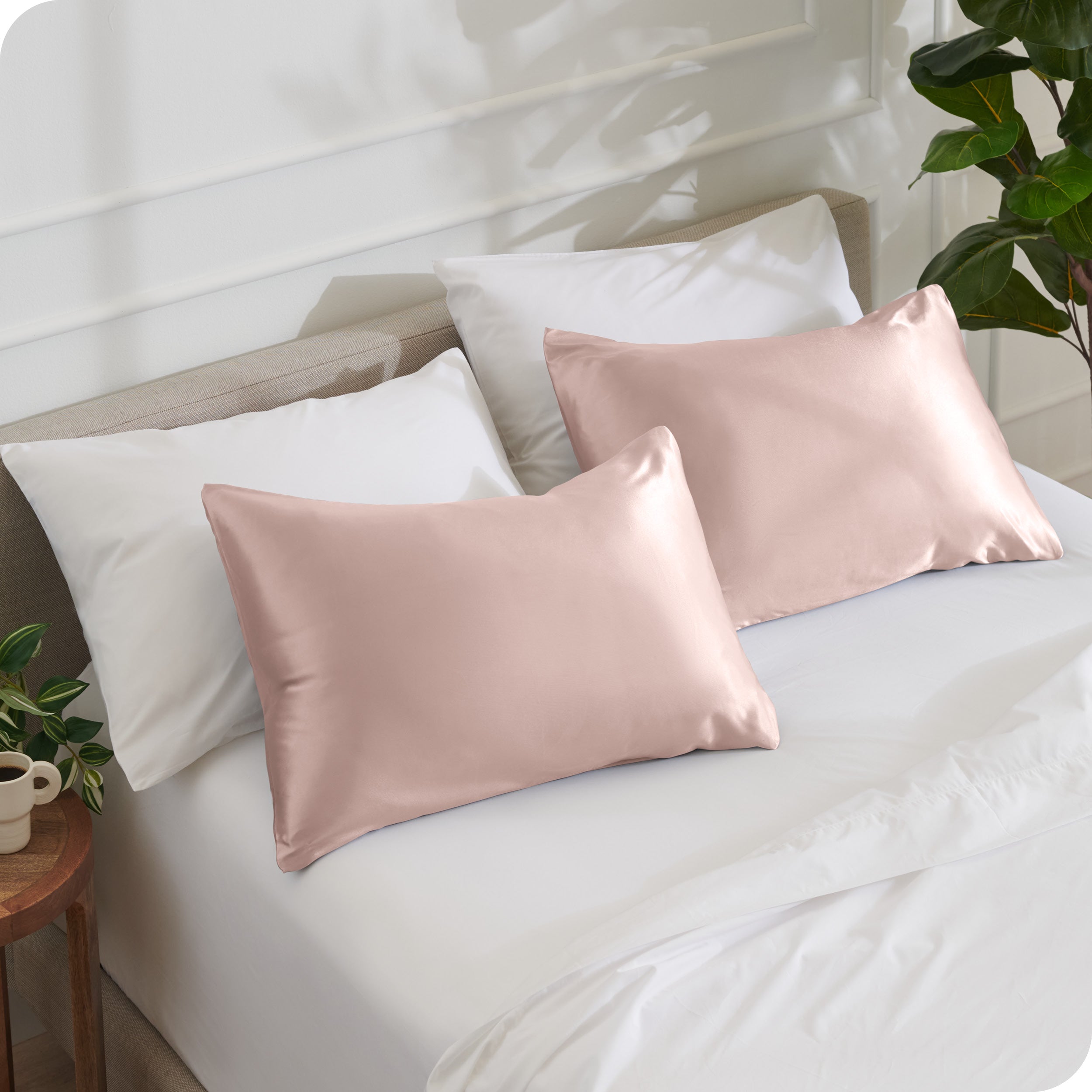 2 satin pillowcases on pillows leaning against other pillows on a bed