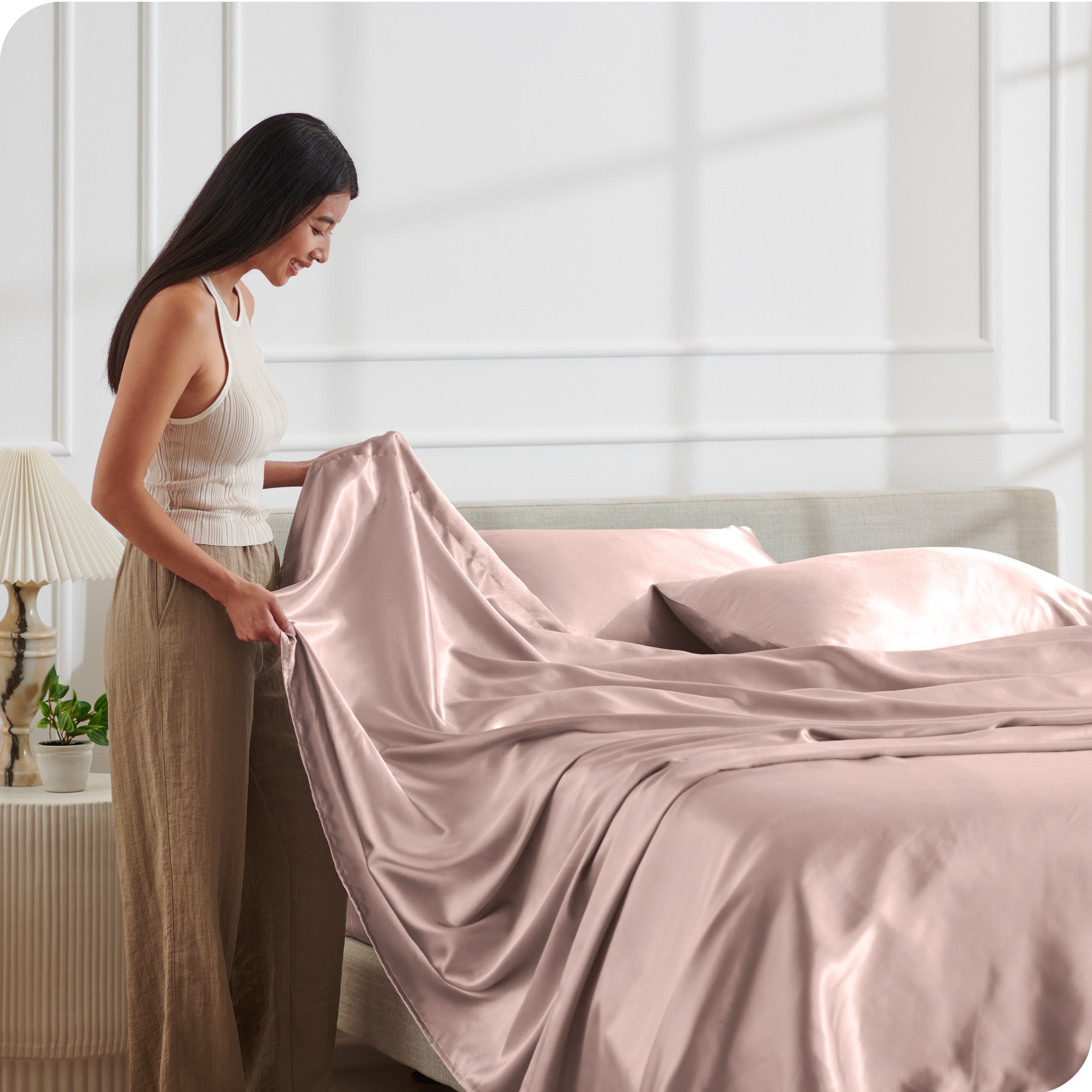 A woman making a bed with satin sheets