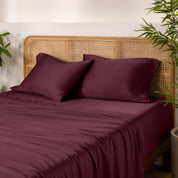 Bamboo bed sheets and pillowcases on a bed with a wicker headboard and plants in the background.