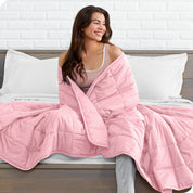 A woman is wrapped in a weighted blanket while sitting on a bed with white sheets.