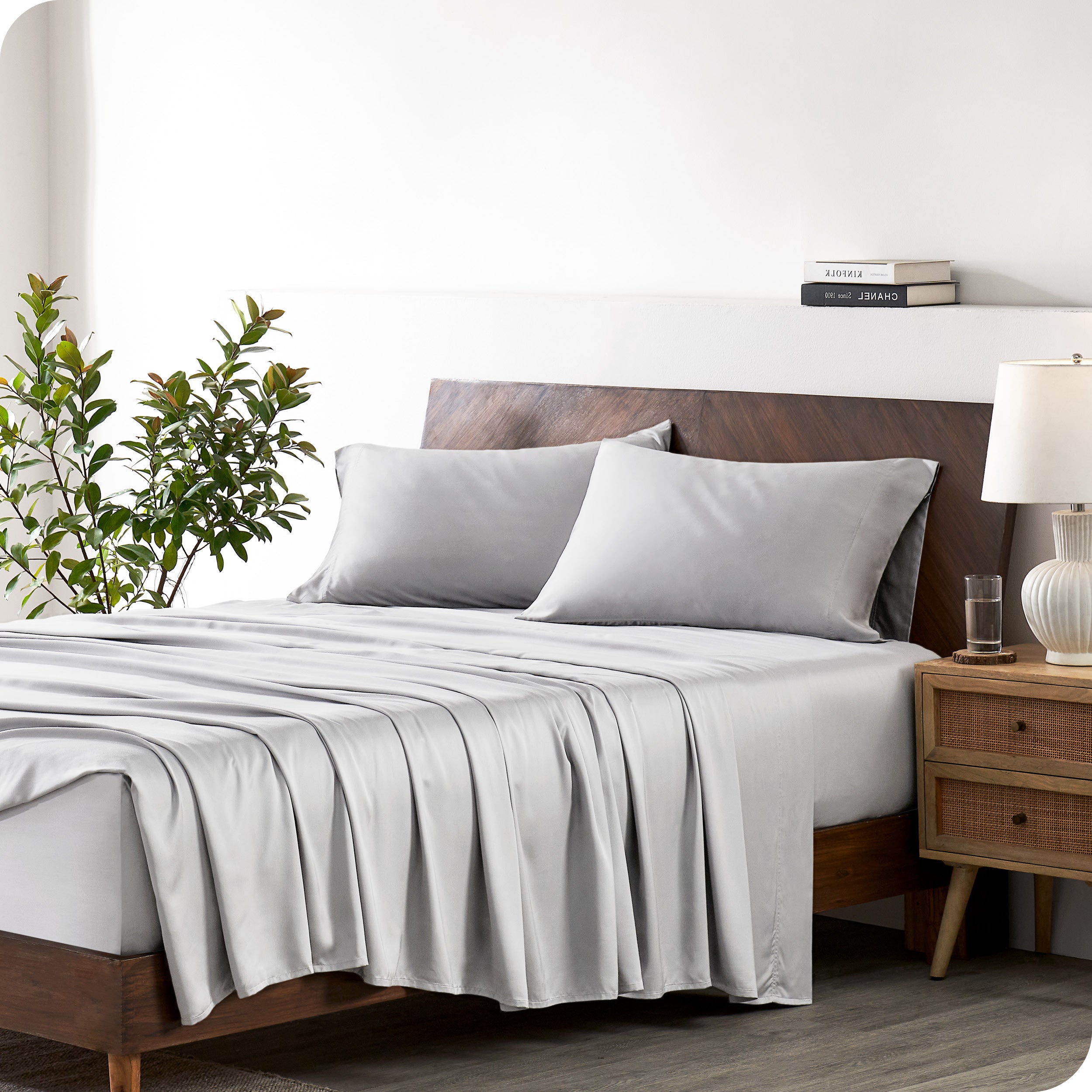 Modern bedroom with a bed against a white wall with a nightstand next to the bed. The bed has bamboo sheets draped over it.