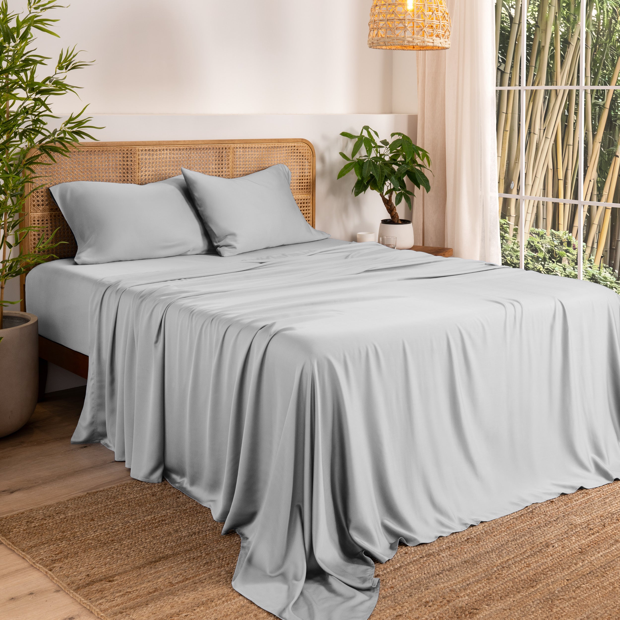 Bamboo sheets on a bed in a bedroom with plants and a window.
