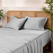 Bamboo bed sheets and pillowcases on a bed with a wicker headboard and plants in the background.