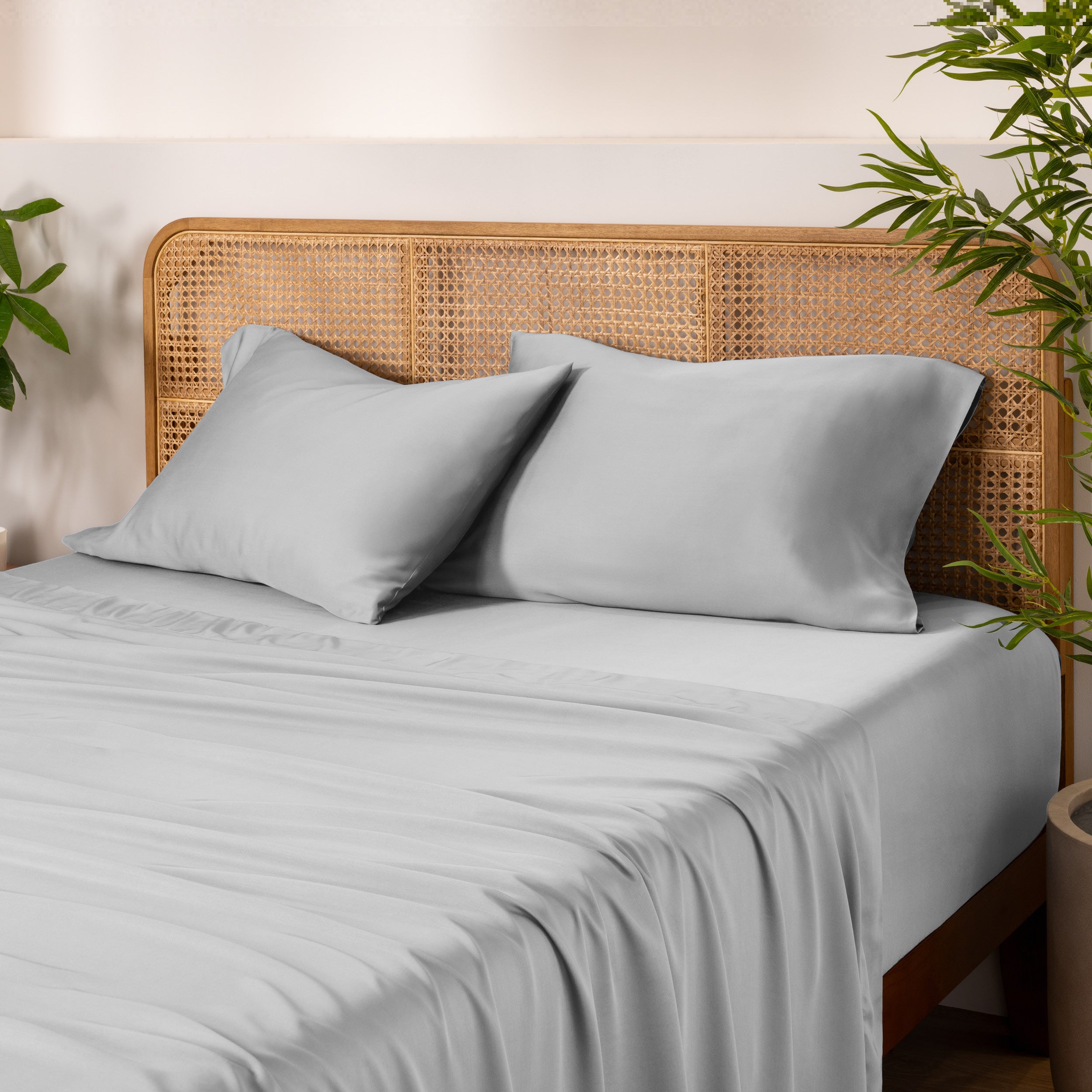 Bamboo bed sheets and pillowcases on a bed with a wicker headboard and plants in the background.