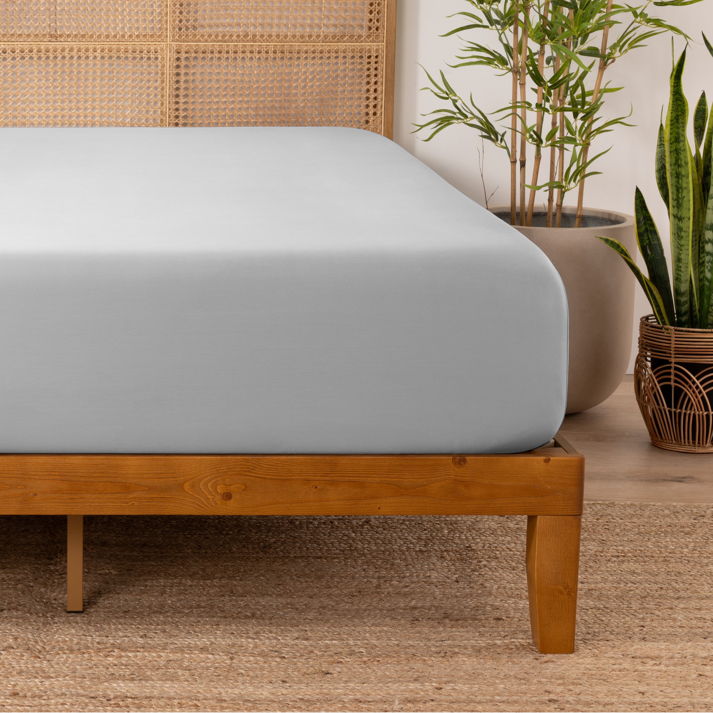 Bamboo fitted sheet on a wooden bed with plants in the background