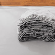 Folded fitted sheet on a bed with a wooden headboard.