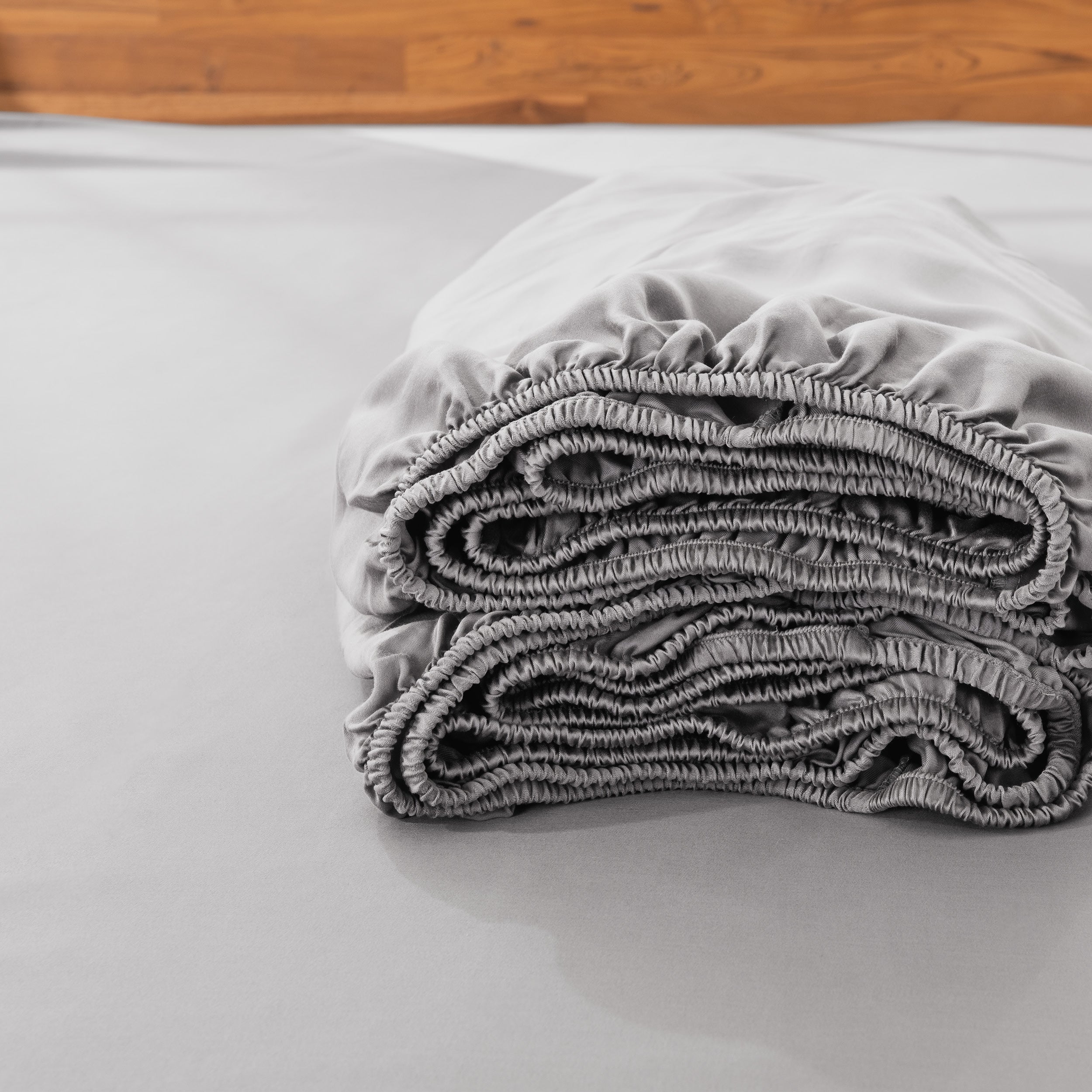 Folded fitted sheet on a bed with a wooden headboard.