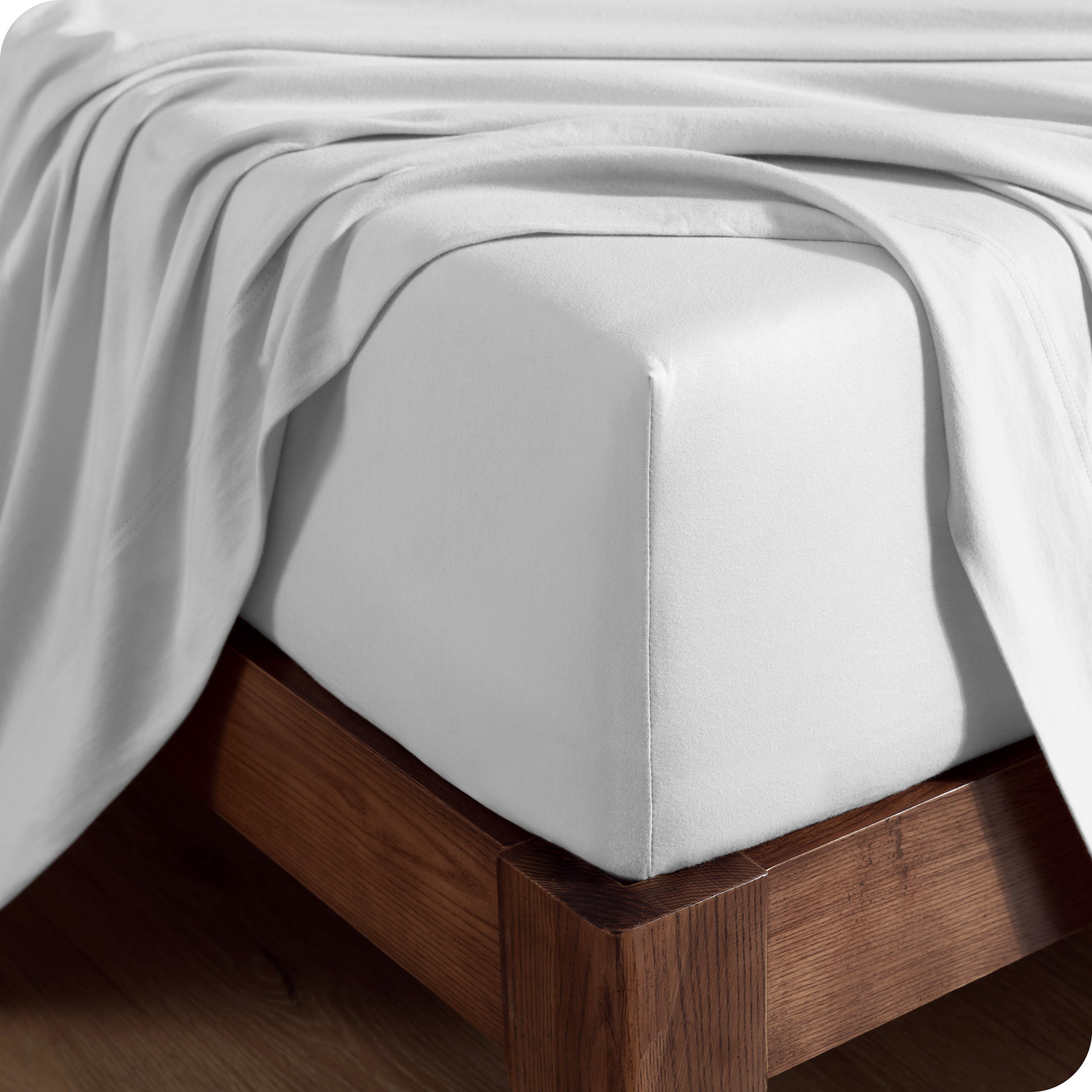 Close up of the corner of a mattress with a fitted sheet and flat sheet on it