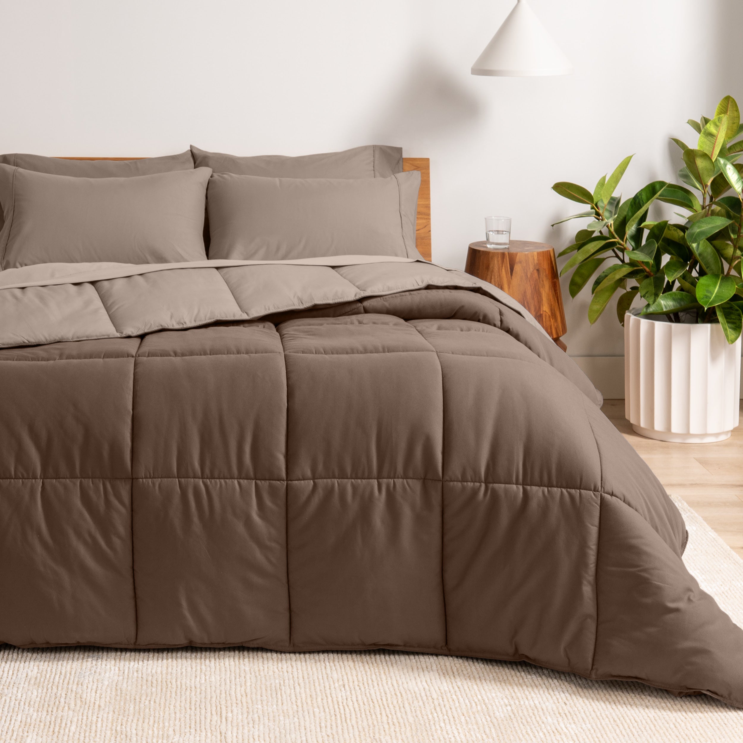 A wooden bed frame with a reversible comforter and sheet set on the mattress in a bright warm room.