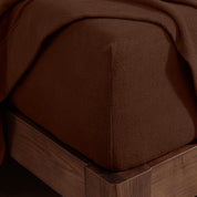 Corner of the bed with a fitted sheet on the mattress and a flat sheet draped over the side and end