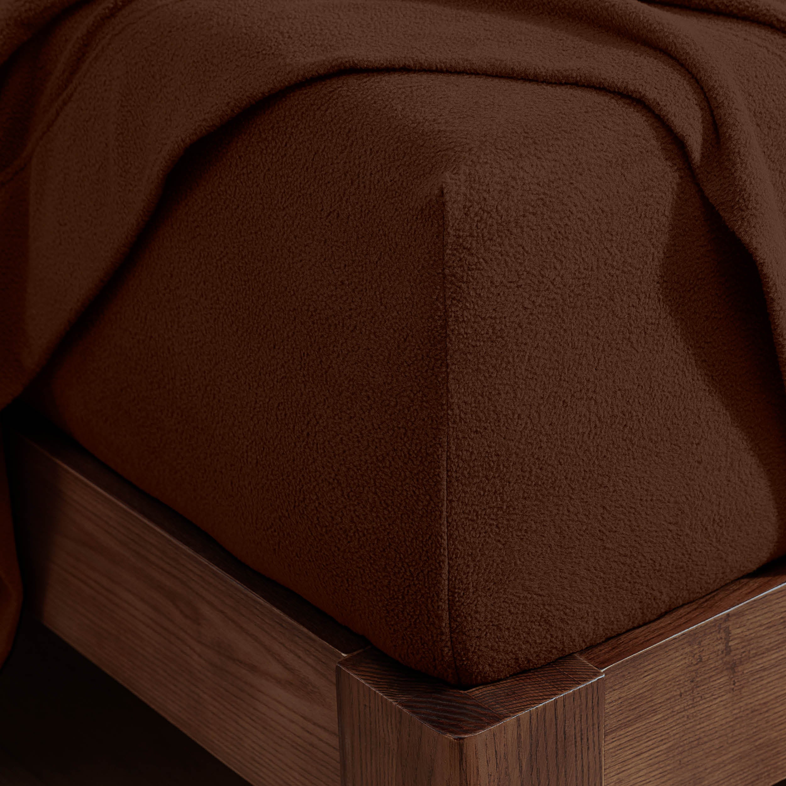 Corner of the bed with a fitted sheet on the mattress and a flat sheet draped over the side and end