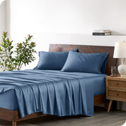 Modern bedroom with a bed against a white wall with a nightstand next to the bed. The bed has bamboo sheets draped over it.