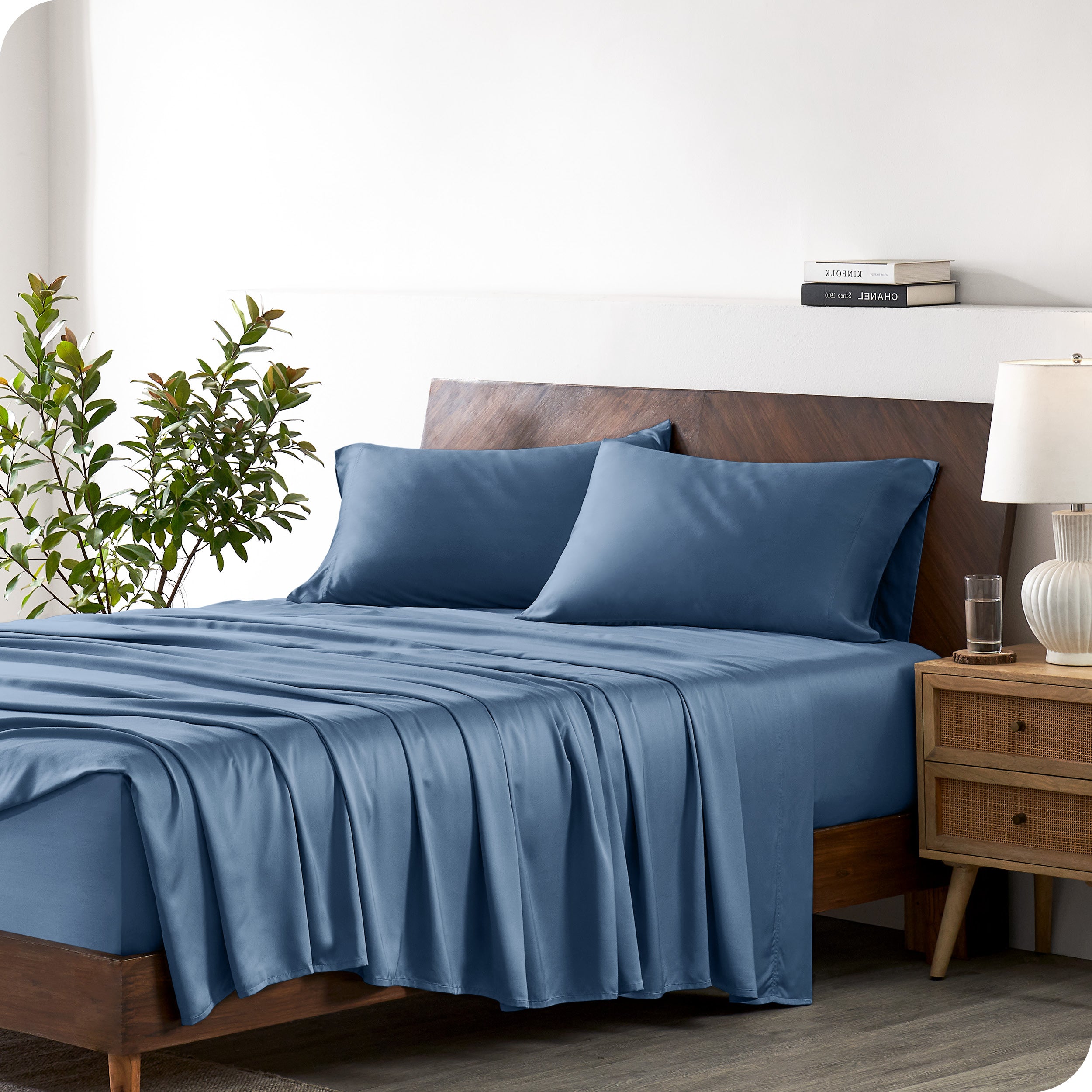 Modern bedroom with a bed against a white wall with a nightstand next to the bed. The bed has bamboo sheets draped over it.
