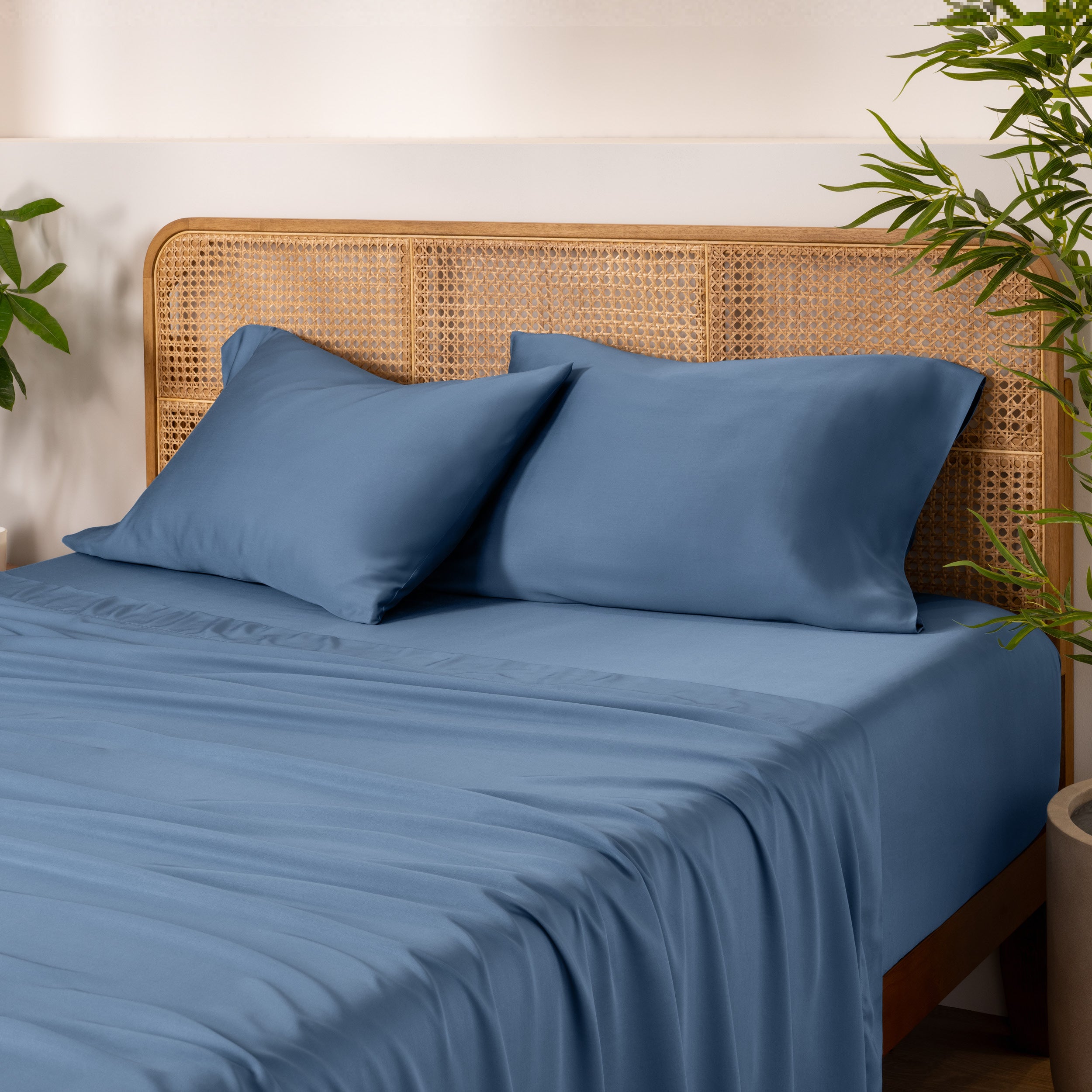 Bamboo bed sheets and pillowcases on a bed with a wicker headboard and plants in the background.