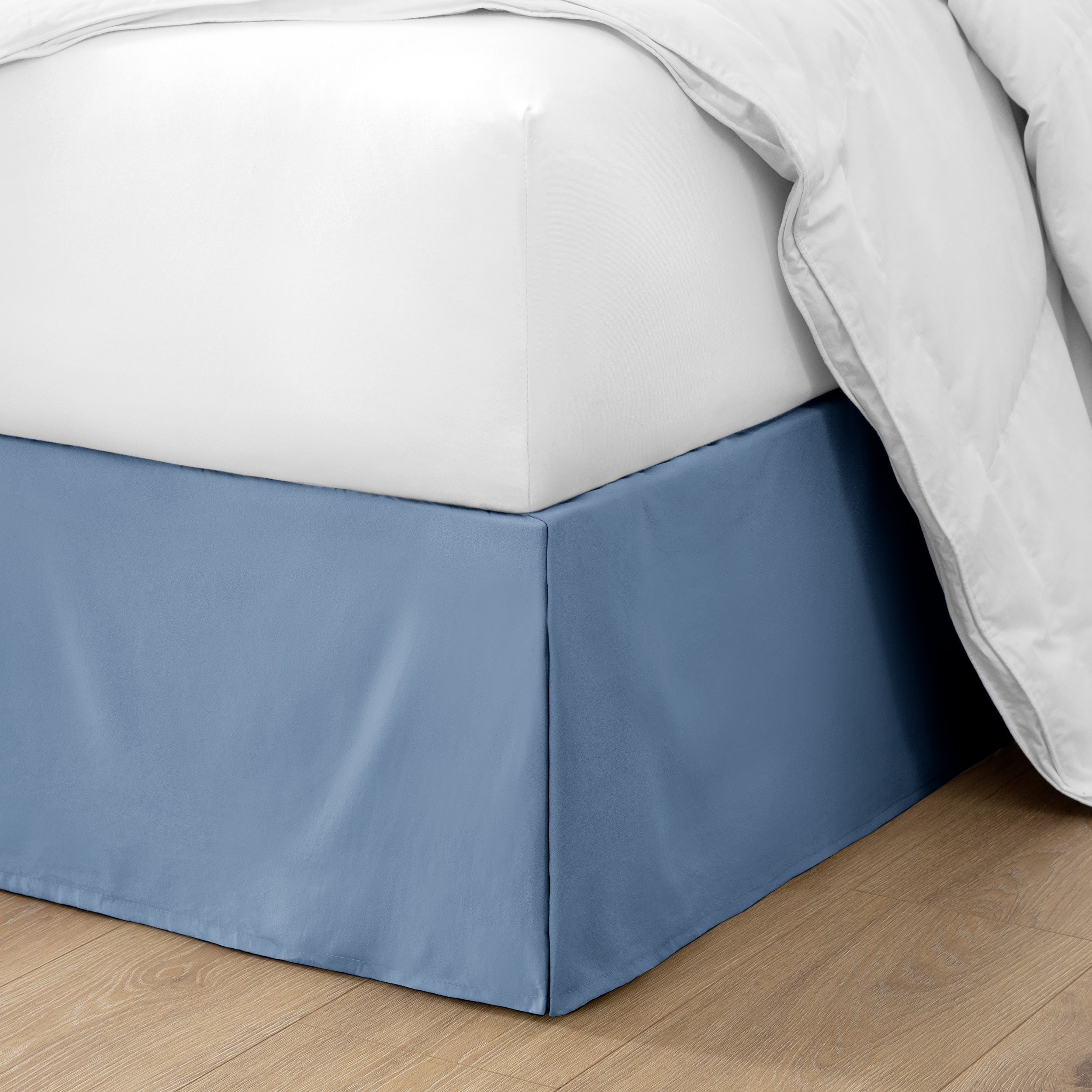 The corner of a bed with a bed skirt and comforter on it