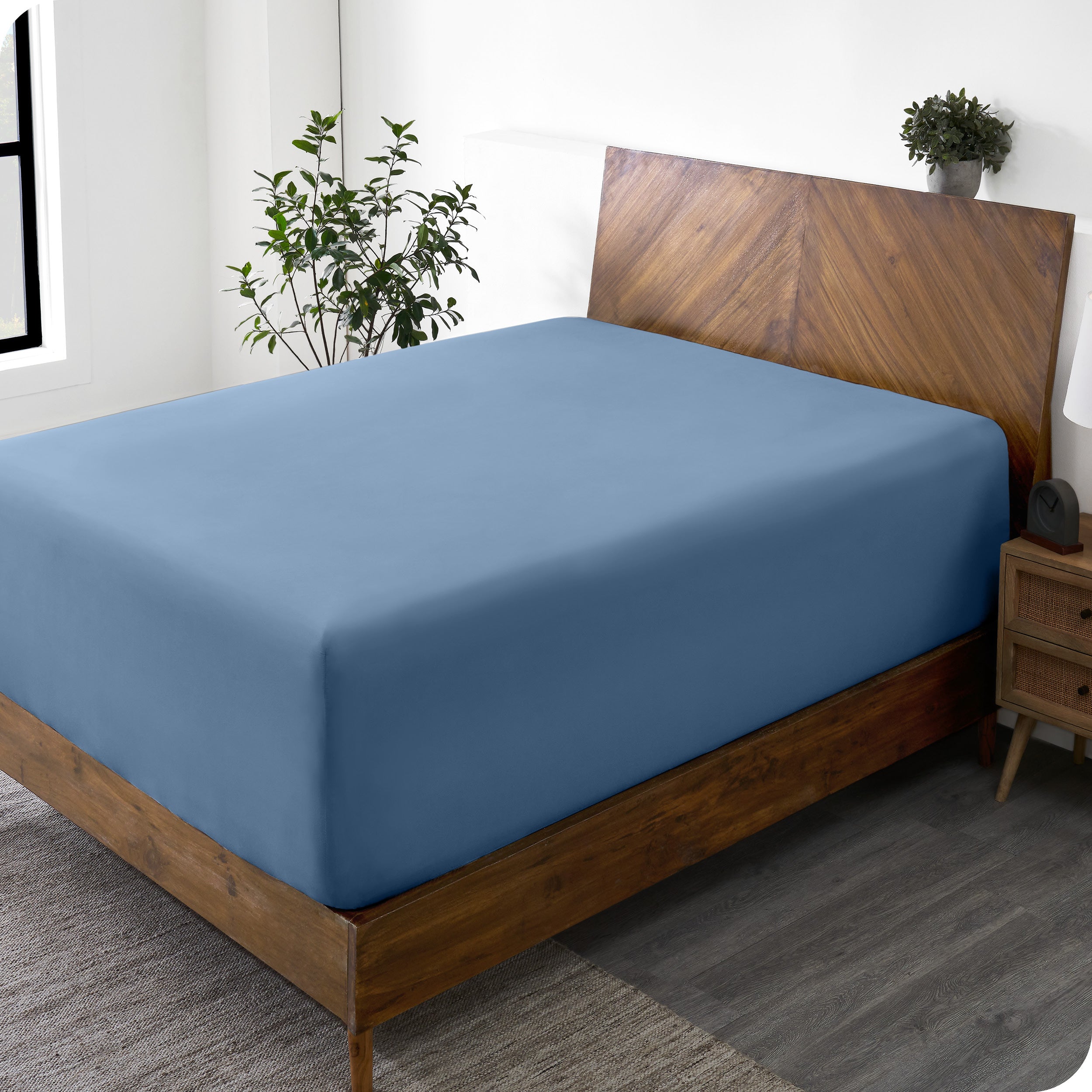 A wide corner view of a modern bed made with a microfiber fitted sheet on the mattress. 