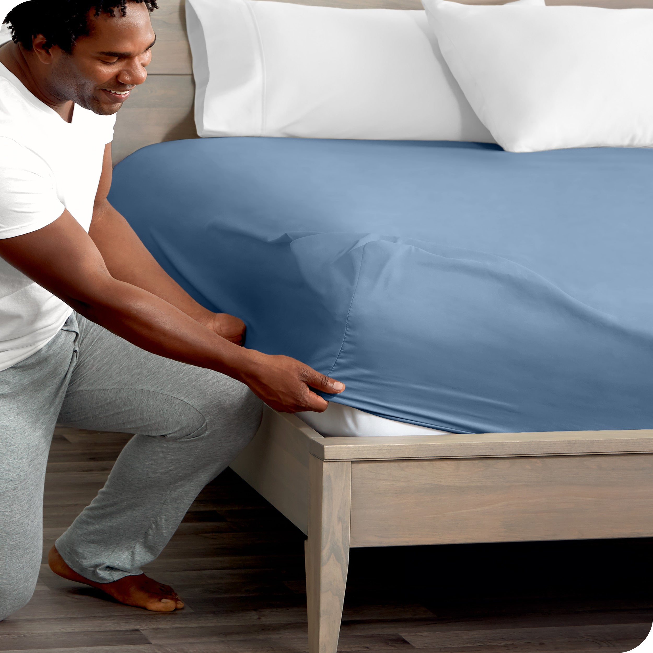 A man kneeling while putting a fitted sheet on a bed