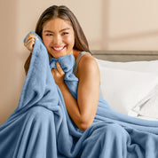 A woman sitting on a bed wrapped in a microplush blanket