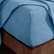 Corner of the bed with a fitted sheet on the mattress and a flat sheet draped over the side and end