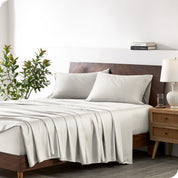 Modern bedroom with a bed against a white wall with a nightstand next to the bed. The bed has bamboo sheets draped over it.