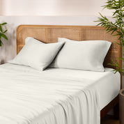 Bamboo bed sheets and pillowcases on a bed with a wicker headboard and plants in the background.