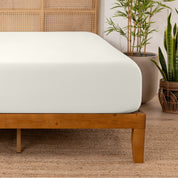 Bamboo fitted sheet on a wooden bed with plants in the background
