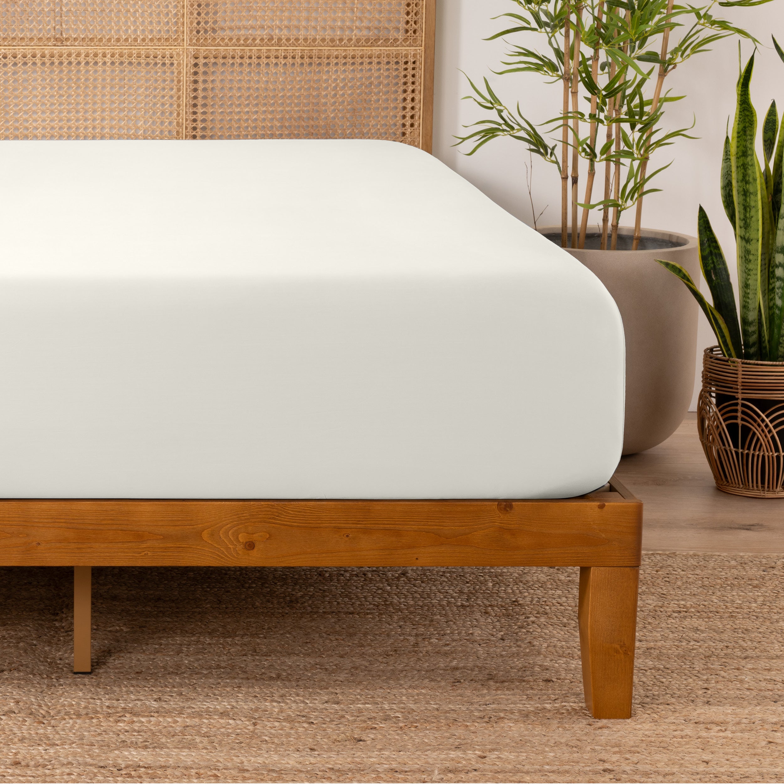 Bamboo fitted sheet on a wooden bed with plants in the background