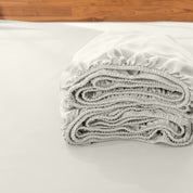 Folded fitted sheet on a bed with a wooden headboard.